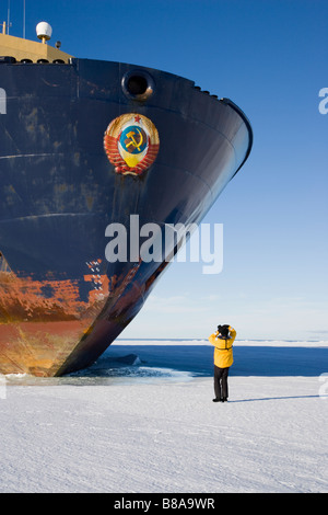 Closeup Small tourist photographer looking up standing in front of big Russian Icebreaker parked in Ice floe Ross Sea Western Antarctic Stock Photo