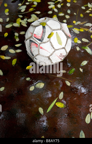 a well worn used deflated football in the rain on a table surrounded by fallen leaves Stock Photo