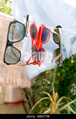 four different retro sunglasses suspended on a washing line in a garden
