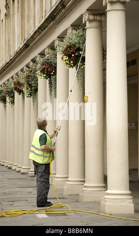Man age 40-50 watering hanging baskets on a regency building in Bath, England. Stock Photo