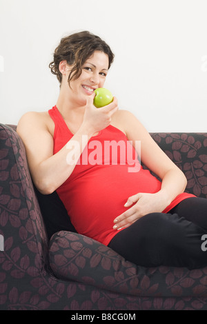 Pregnant woman eating apple on sofa, portrait