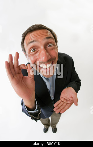 Fish eye lens of a man with a silly grin on white background giving the OK hand gesture Stock Photo