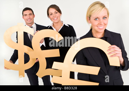 Studio concept shot showing business people standing in a line carrying giant golden Dollar Pound Sterling and Euro symbols Stock Photo