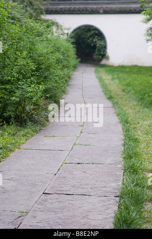 stone garden path leading to an arched doorway through a white wall Stock Photo