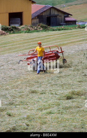 Teen boy operates rake machine that turns the grass on his farm in Switzerland Stock Photo