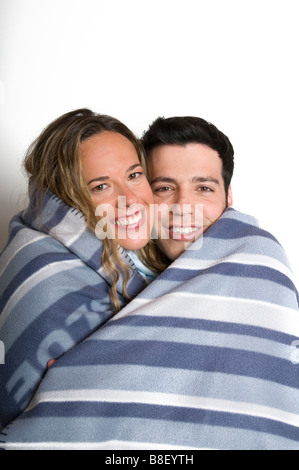 A young romantic couple in their 20s wrapped together in a blanket on a white background Model Releases available Stock Photo
