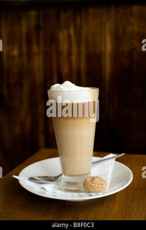 Cafe Latte in a clear glass with an almond cookie agains dark brown wood background Stock Photo
