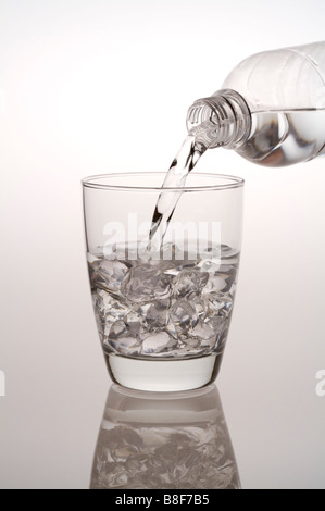 Water being poured from a water bottle into a glass filled with ice cubes Stock Photo