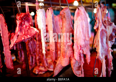 Pieces of raw pork hanging from metal hooks in a market stall Stock Photo