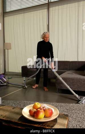 Senior woman vacuum-cleaning the floor of a modern appartment Stock Photo