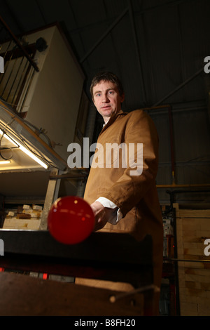 a professional glass blower takes some molten glass out of a furnace ready to blow and shape into a vase or glass ornament Stock Photo