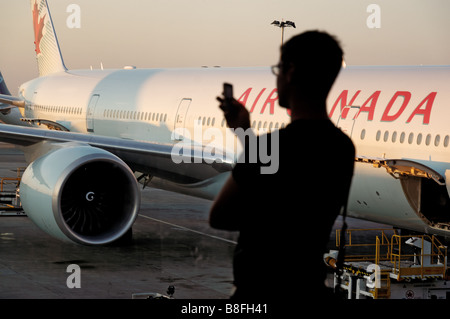 A man on a mobile phone in silhouette in an airport departure lounge window with a plane behind Stock Photo