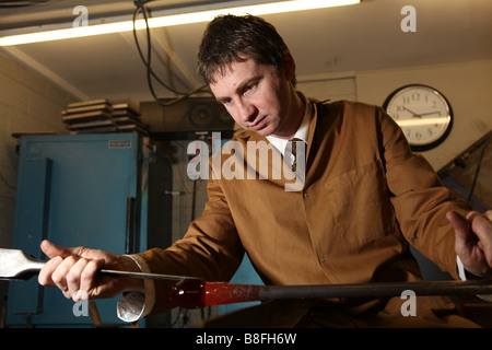 a professional glass blower takes some molten glass out of a furnace ready to blow and shape into a vase or glass ornament Stock Photo