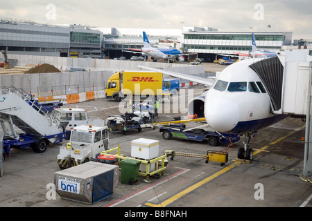 Baggage handlers and vehicles around a A BMI plane on the tarmac at Terminal 1, Heathrow airport, London, UK Stock Photo