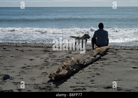 Man and Dog sitting on Beach Hokitika New Zealand Stock Photo