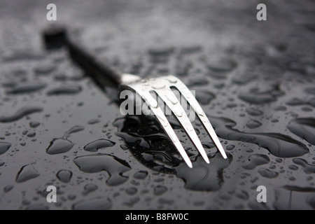 A dinner fork on a smooth metal surface with rain drops Stock Photo