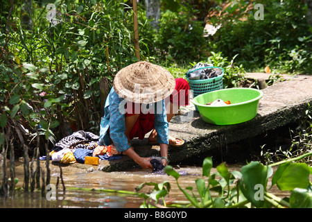 Vietnamese woman with the traditional conical hat doing her laundry in the river. Mekong delta region. Vietnam South East Asia Stock Photo