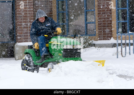 John Deere riding lawn mower fitted with a snow plow removing snow from a parking lot in Boise Idaho USA Stock Photo