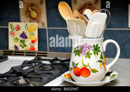 A large, decorated pitcher holding kitchen utensils next to a gas burning range. USA Stock Photo