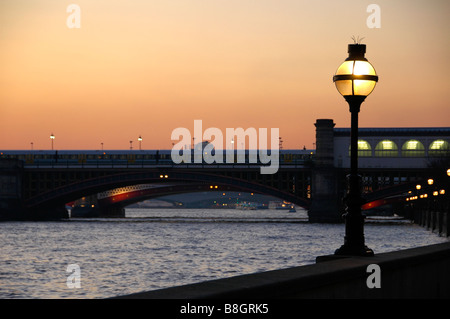 An ornate lamp against a sunset sky on Victoria Embankment with Blackfriars Bridge in the background, London, England, UK Stock Photo