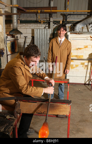 a professional glass blower takes some molten glass out of a furnace ready to blow and shape into a vase or glass ornament Stock Photo