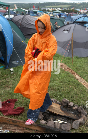 Glastonbury Festival 2007, teenage girl stands in campsite in bad weather wearing free Orange rain mac Stock Photo