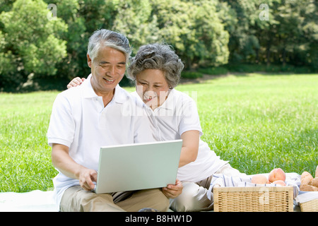 Senior couple using laptop while having picnic Stock Photo