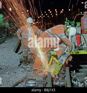 Contractor working at night using abrasive disc machine cuts lengths of worn-out rail during a trackwork upgrading programme. Stock Photo