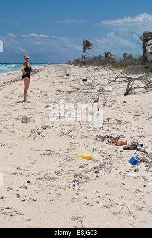 Plastic trash washed ashore on the white sand beach near Tulum Mexico with tourist. Stock Photo