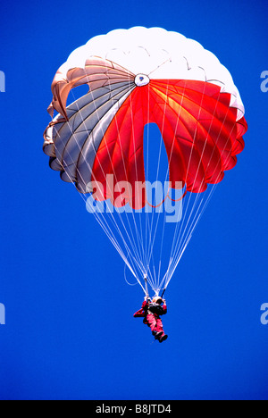 One Sky Diver skydiving with a Red and White Parachute in a Blue Sky Stock Photo
