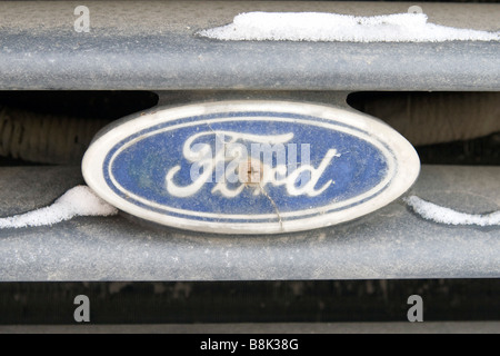 Dusty and snow covered falling off Ford logotype screwed on to the car grille. Stock Photo
