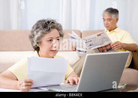 Mature woman using laptop while senior man reading newspaper in sofa Stock Photo