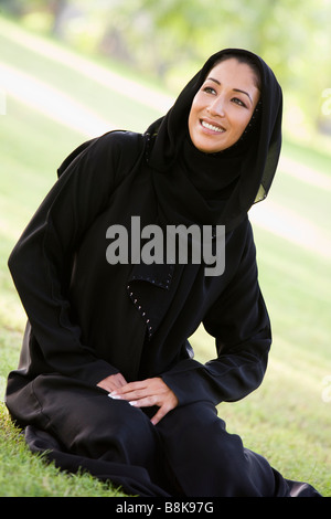 Woman sitting outdoors in park smiling (selective focus) Stock Photo