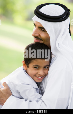 Man and young boy outdoors in park embracing and smiling (selective focus) Stock Photo