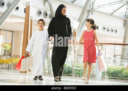 Woman and two young children walking in mall holding hands and smiling (selective focus) Stock Photo