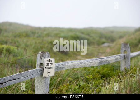 A sign reading 'Please keep off the dunes' on a weather beaten fence on an overcast day. Stock Photo