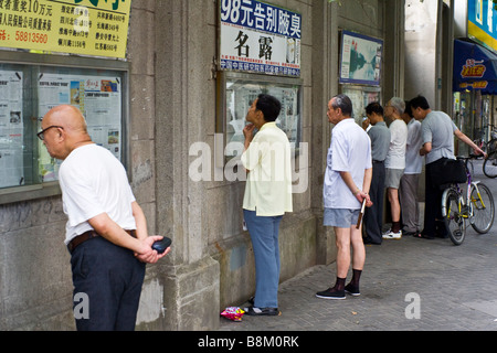 Concentrating on the latest news on an outdoor newspaper display board on a street in Shanghai, China. Stock Photo