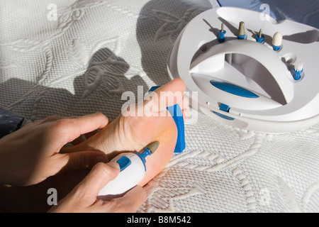 Woman removing corn on her foot with home pedicure set Stock Photo