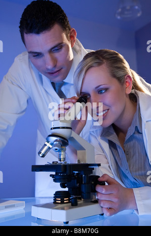 A female medical or scientific researcher using her microscope and laptop behind her is a male colleague Stock Photo