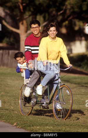 Hispanic mother and father give young son a ride on back of a tandem bicycle in park Stock Photo