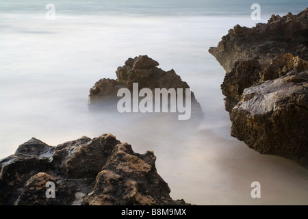 long exposure used on waves around coastal rocks to produce moody misty effect Stock Photo