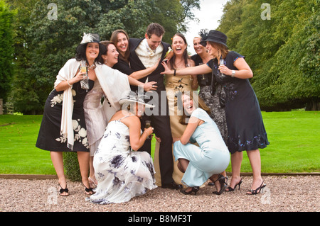 Horizontal informal group portrait of a groom on his wedding day being man handled and tickled by close female friends Stock Photo