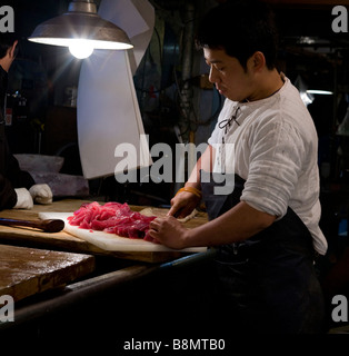 Fish market worker cutting up tuna for sushi and sashimi at Tokyo Metropolitan Central Wholesale Market Tsukiji Fish Market Stock Photo