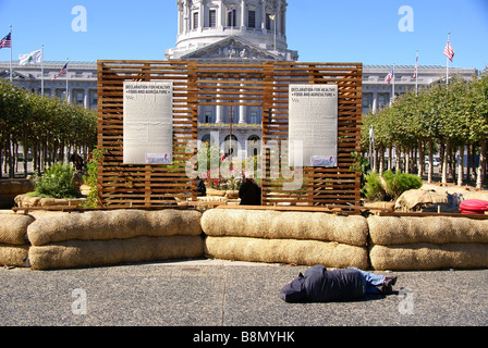 Homeless person sleeps in front of 'Declaration for healthy food and agriculture' sign by city hall in San Francisco Stock Photo
