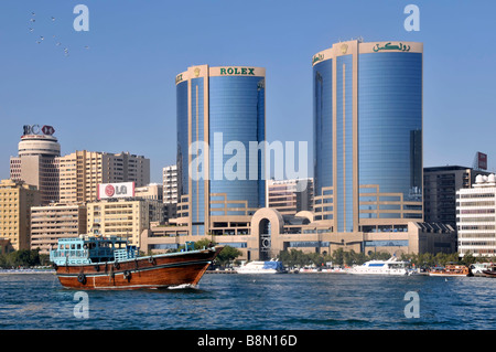 Dubai twin towers with Rolex advert & modern building architecture urban skyline close up of passing dhow boat on Dubai Creek UAE Middle East Asia Stock Photo