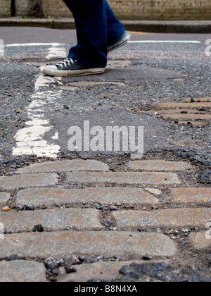 Old cobblestones show through holes in road tarmac. Stock Photo