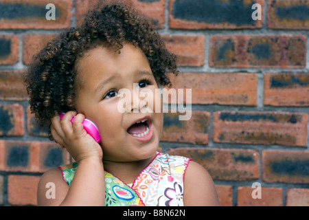 Mixed race 4yr old girl with curly hair holding imaginary conversation on a toy mobile phone Stock Photo