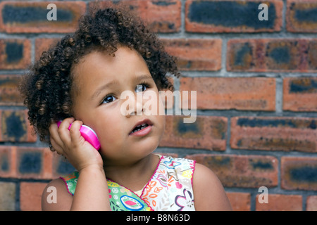 Mixed race 4yr old girl with curly hair holding imaginary conversation on a toy mobile phone Stock Photo