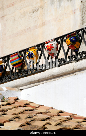 Spanish ceramic pots hang on a iron railing above a tiled roof in the town of Frigiliana southern Spain Stock Photo