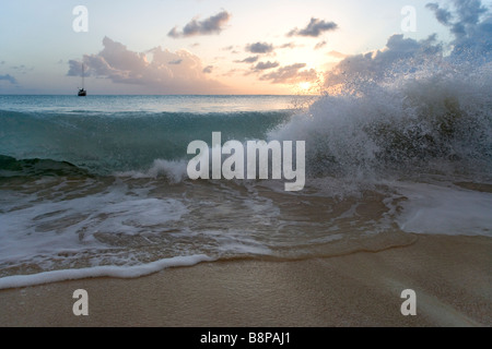 A cruising Sailboat anchored off 11 mile beach at sunset as a wave breaks on the beach Stock Photo